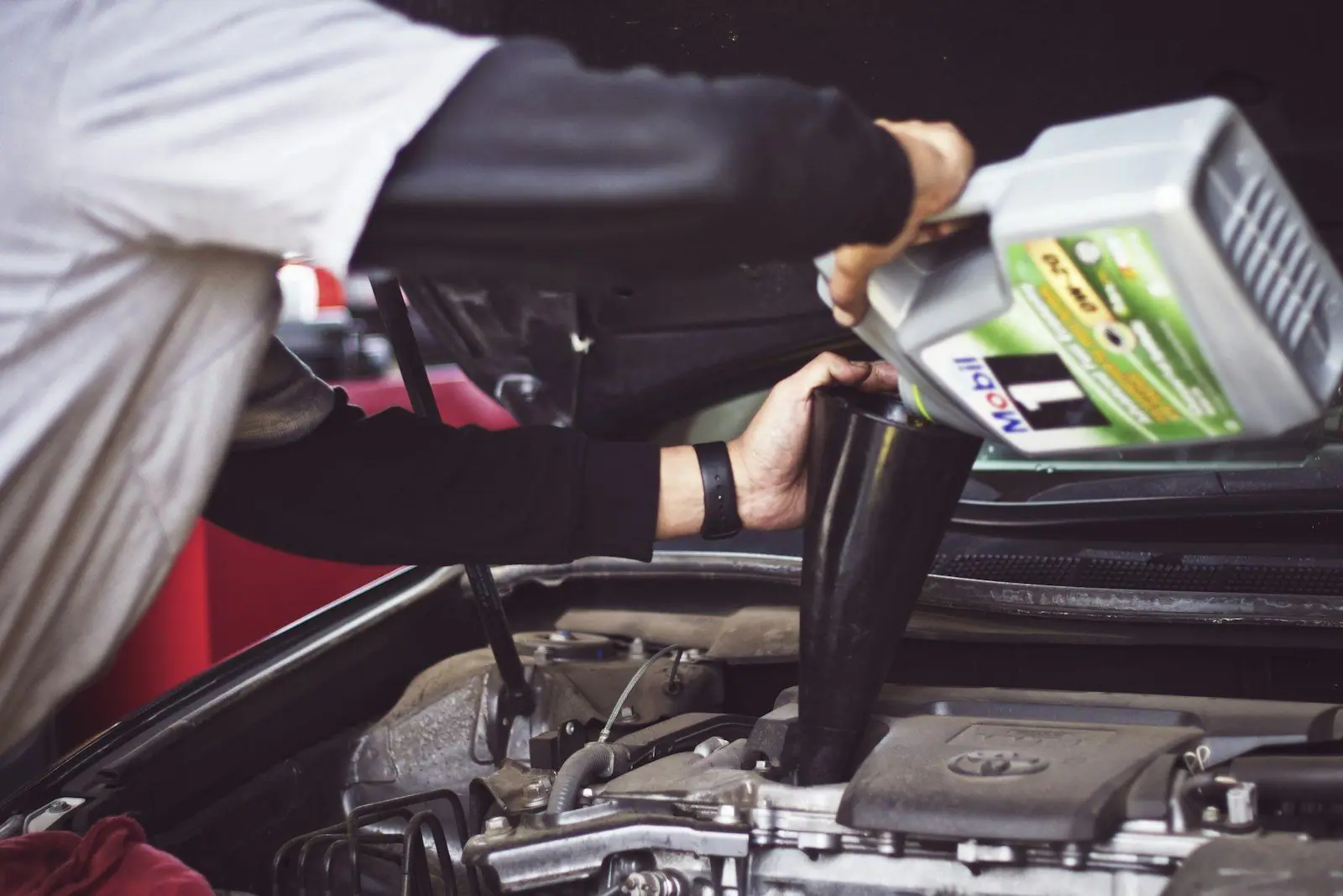 A mechanic pouring engine oil through a funnel under the open bonnet of a car